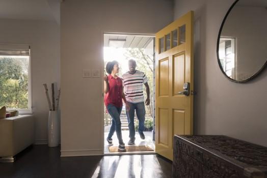 Young man and woman stepping into the house, they are happy and smiling as they come through the open yellow door