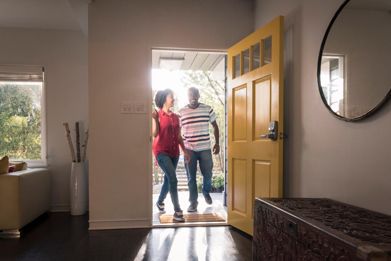 Young man and woman stepping into the house, they are happy and smiling as they come through the open yellow door